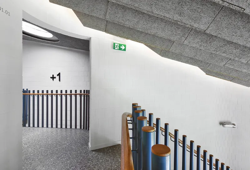Curved white wall with vertical blue and wood handrail detailing and exit signage overhead