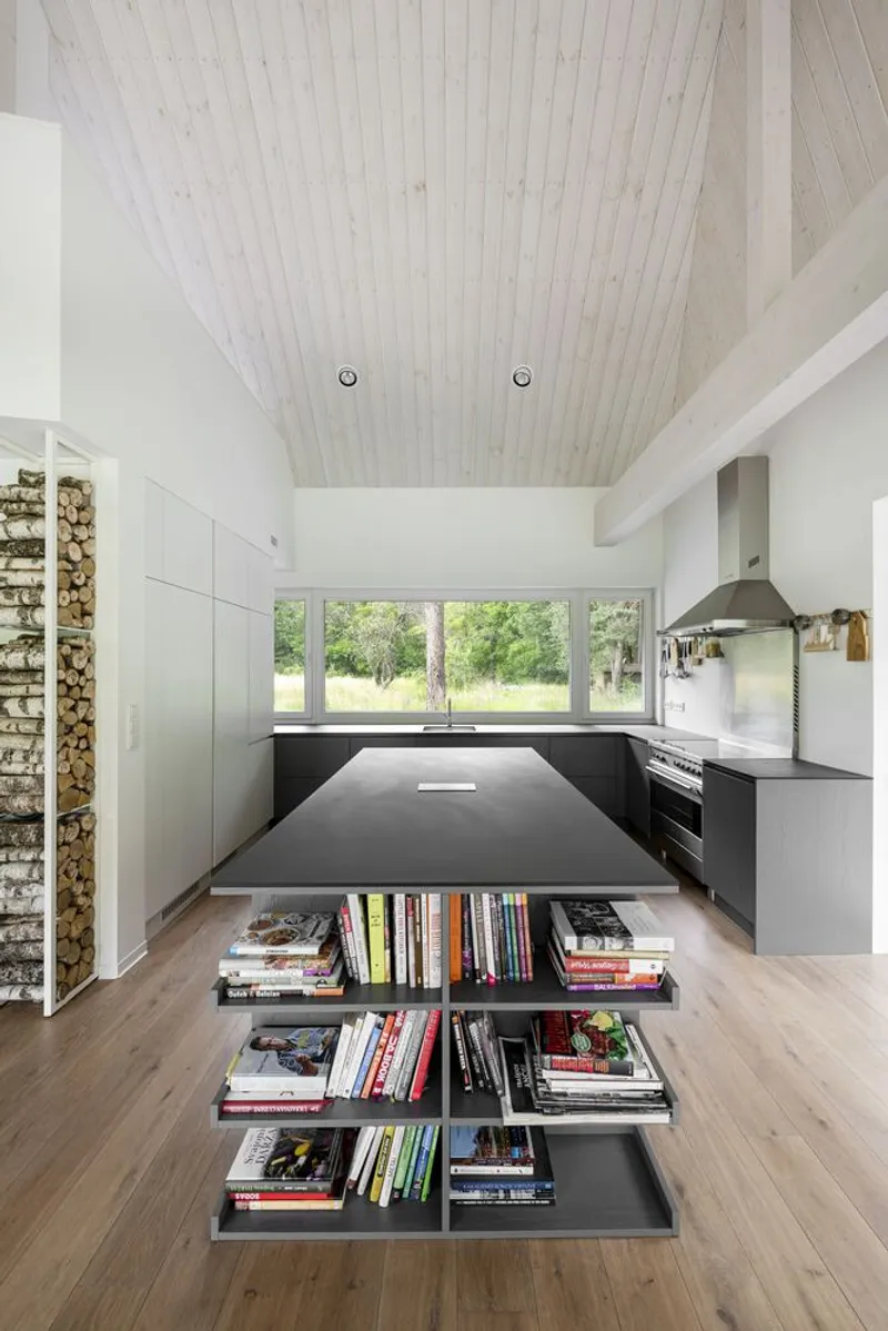 Kitchen island with integrated book shelving beneath a pale wood paneled vaulted ceiling