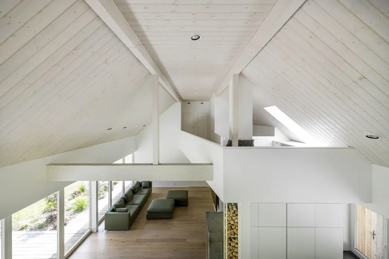 Double-height living room viewed from upper level mezzanine with exposed timber ceiling beams and diagonal planking