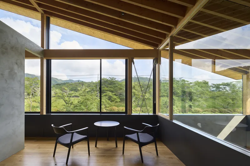 Seating nook with timber floor, two chairs and a small table overlooking green landscape through tall windows