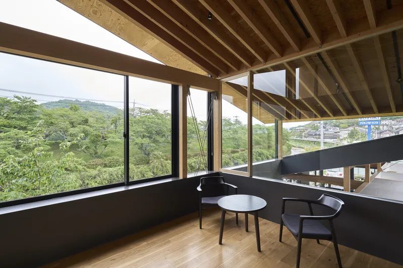 Interior mezzanine with exposed timber joists, full-height glazing overlooking forested hillside and black metal railing