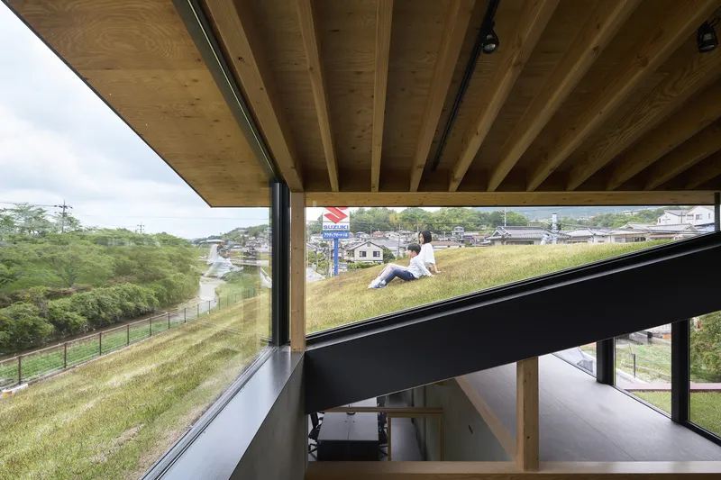 View beneath the cantilevered timber soffit showing person on planted green roof with hillside neighborhood beyond