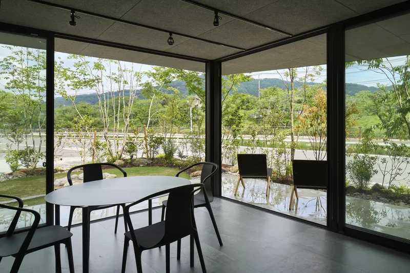 Glazed corner room with sliding doors opening to gravel courtyard planted with birch trees and distant mountains