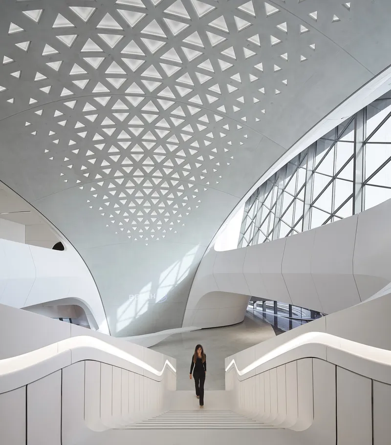 White staircase rising beneath a triangular perforated ceiling pattern with a person descending the steps