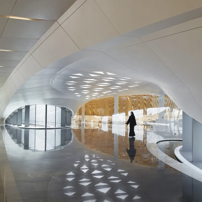 Interior atrium with vaulted ceiling, perforated oculus and a figure reflected on polished dark stone floor