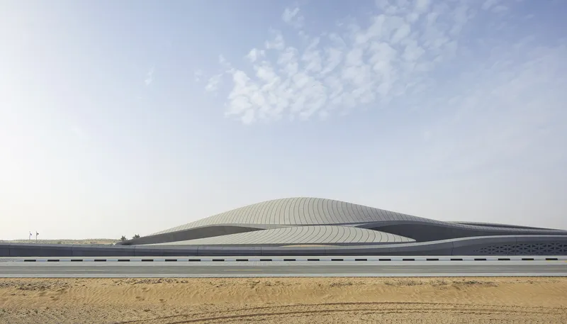 Long ribbed roof structure rising from a flat desert landscape under a cloudy sky