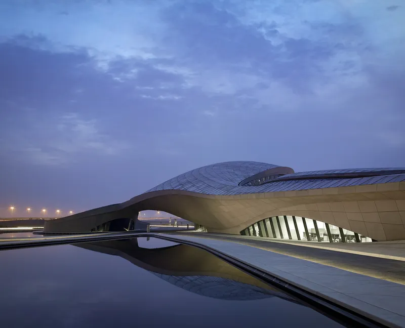 Arched entrance canopy and reflecting pool at dusk with street lights glowing in the distance