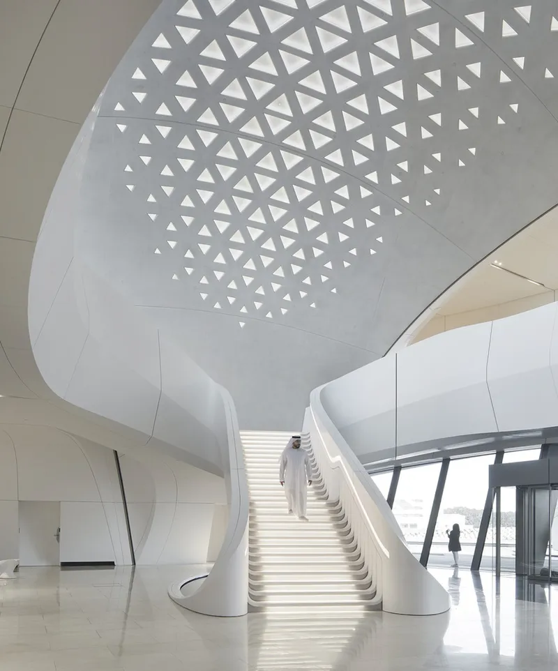 Illuminated staircase ascending beneath a domed ceiling with triangular openings and a figure in white