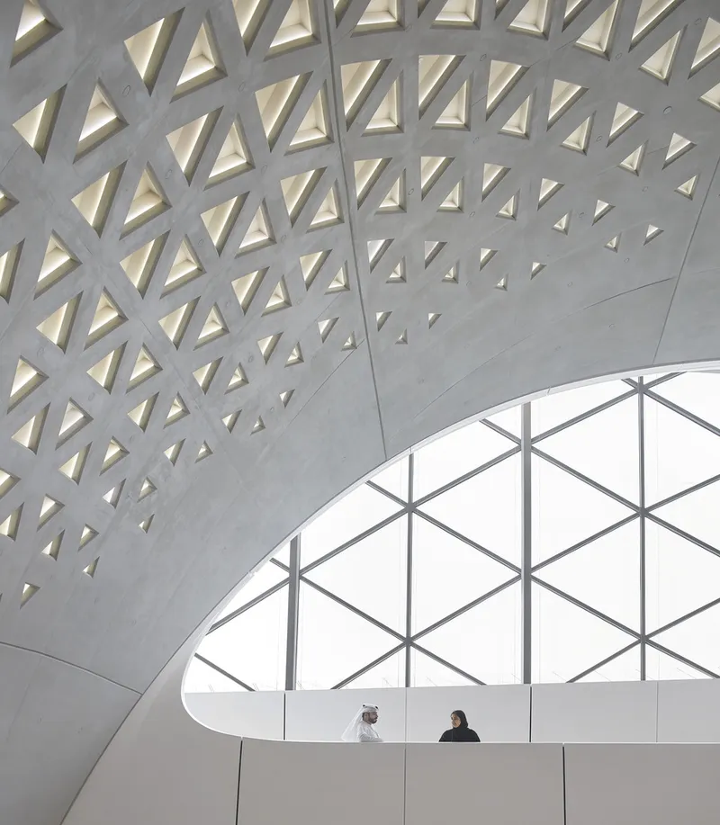Interior atrium with triangular perforations in the concrete ceiling and two figures at a curved balcony