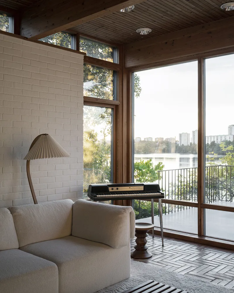 Living room corner with white brick wall and timber ceiling overlooking a lake through full-height glazing