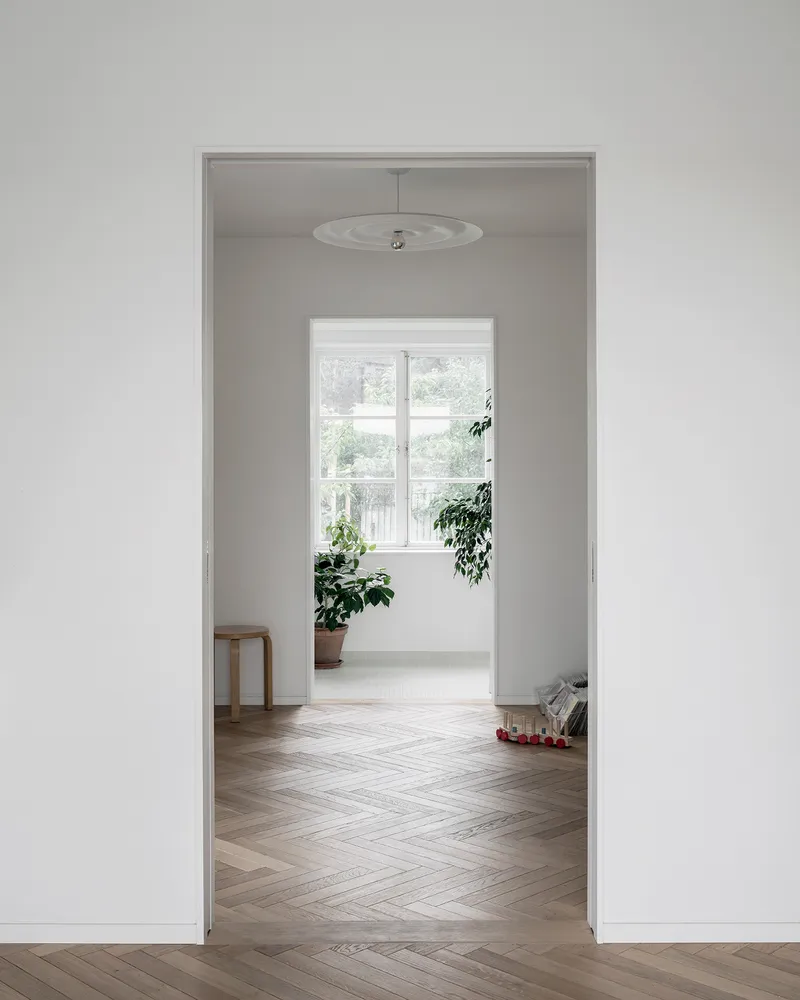 Doorway framing a room with herringbone wood flooring and a window overlooking green foliage