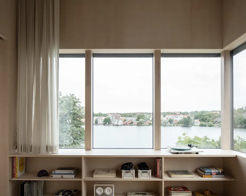 Built-in shelving below a glazed window wall with timber mullions overlooking a lake and distant shoreline