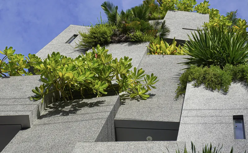 Close-up of the stepped facade planters with textured aggregate finish supporting various tropical plantings under blue sky