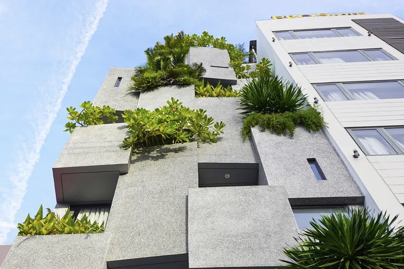 Upward view of the terraced concrete facade with planted beds filled with palms and succulents against clear sky