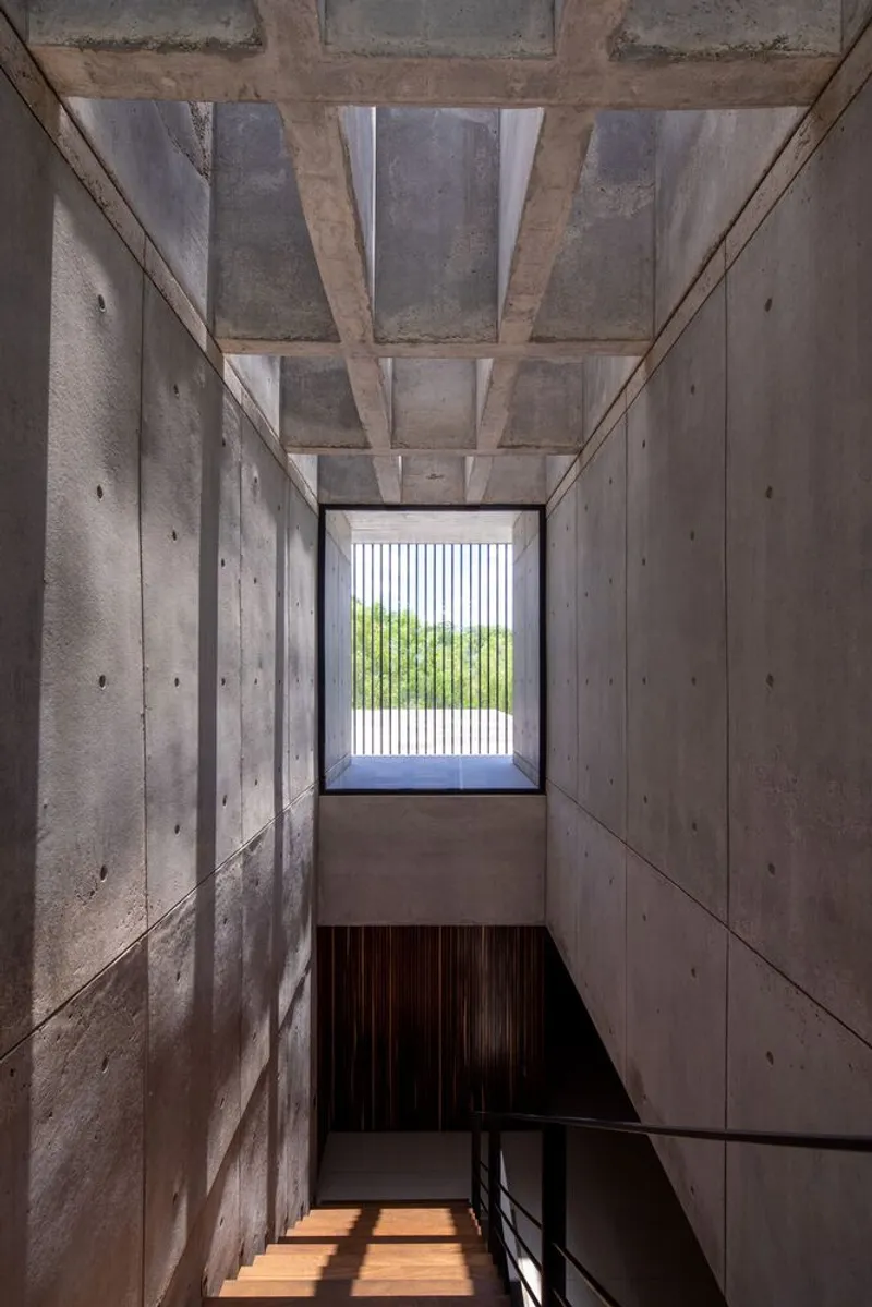 Concrete stairwell with board-formed walls and exposed beam ceiling looking toward screened window opening