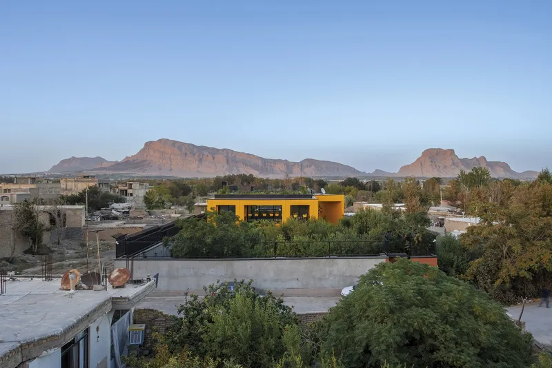 Elevated view of the yellow roof volume rising above neighboring rooftops with red mesa cliffs beyond