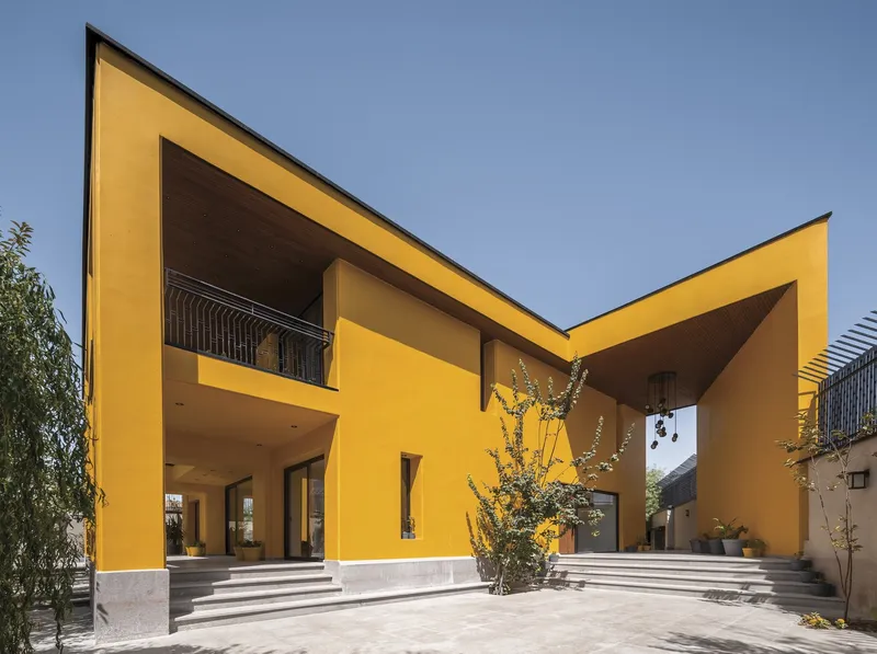 Courtyard entry with yellow rendered walls, angled rooflines and stone steps framing a planted threshold