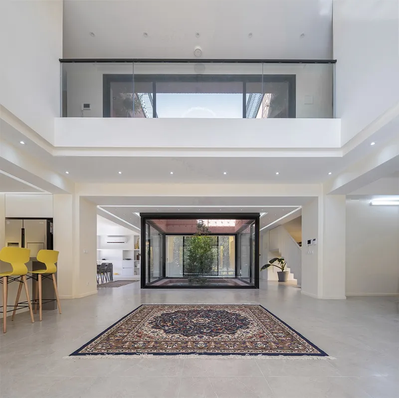 Double-height interior hall with glass-enclosed courtyard and traditional patterned rug on polished tile floor