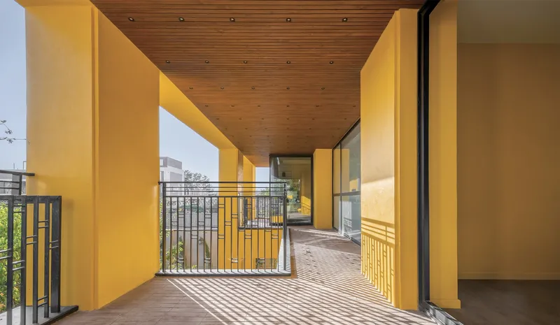 Upper-level balcony with timber slat ceiling and yellow plaster walls casting striped afternoon shadows