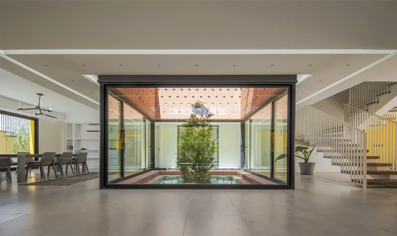 Interior view through black-framed glazing toward the timber-clad courtyard roof with perforated skylight panels
