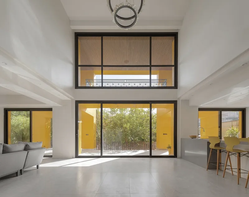 Living space with stacked horizontal windows framing yellow exterior walls and courtyard trees in daylight