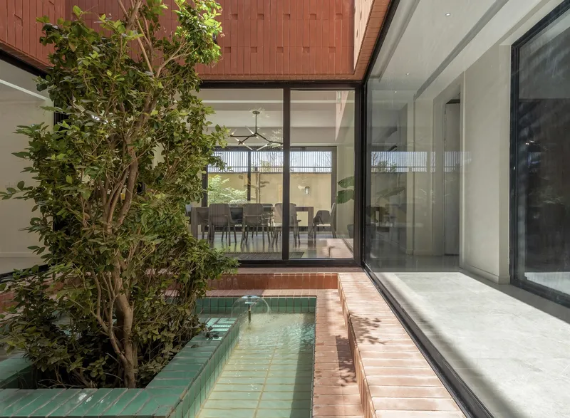 Interior courtyard with green tiled water feature and planted tree framed by sliding glass walls