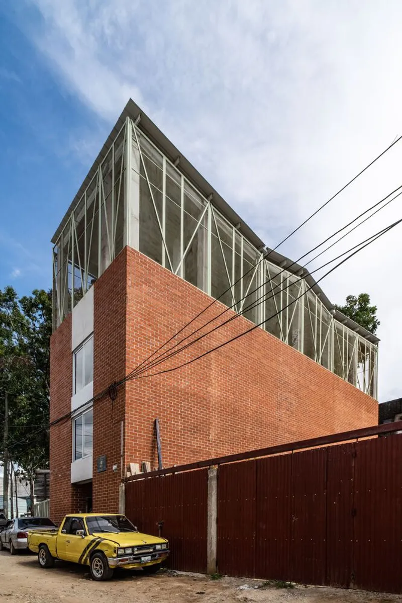 Corner elevation showing the red brick base and diagonal-braced glass upper story with a yellow pickup truck parked outside