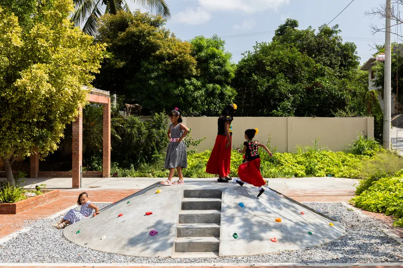 Sloped concrete climbing wall with handholds and steps where children play in dappled sunlight