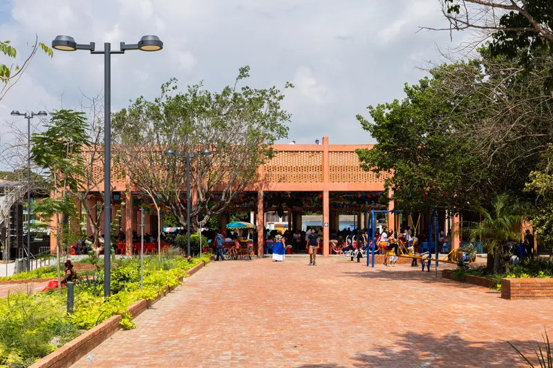 Frontal view of the open-air pavilion with perforated brick screen and visitors gathering on brick-paved plaza