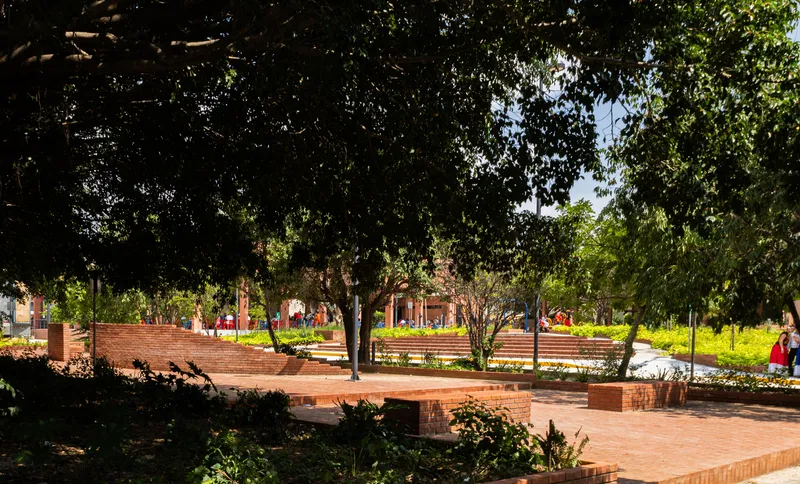 Brick plaza with stepped seating terraces and planted beds beneath established tree canopy