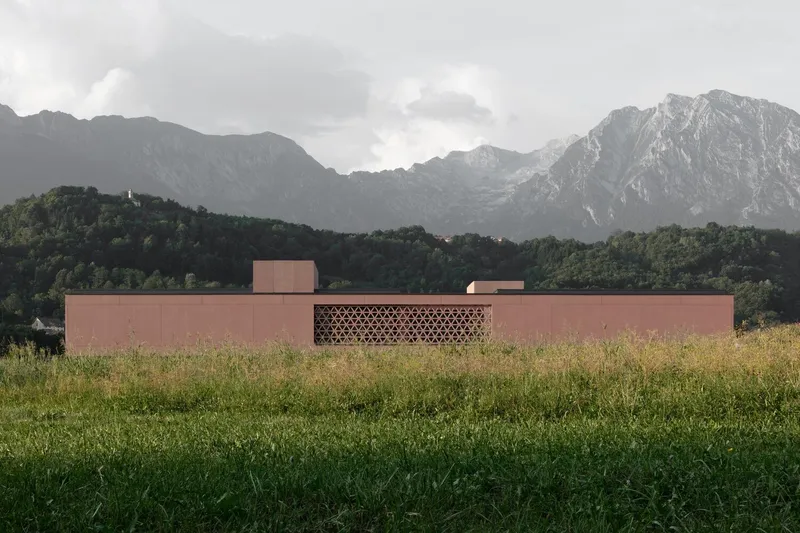 Perforated panel facade centered in the long elevation viewed across an open meadow