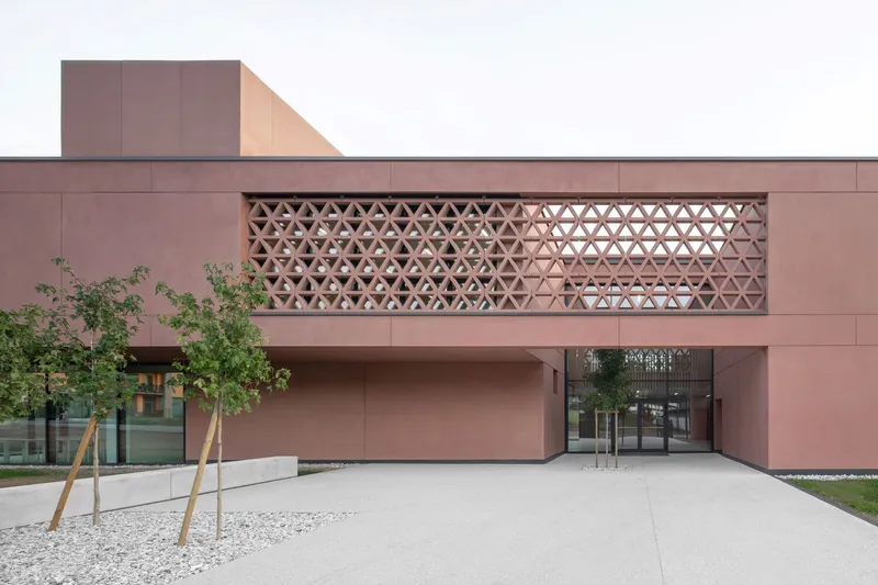 Entry approach showing the latticed opening above glass doors with young trees in gravel