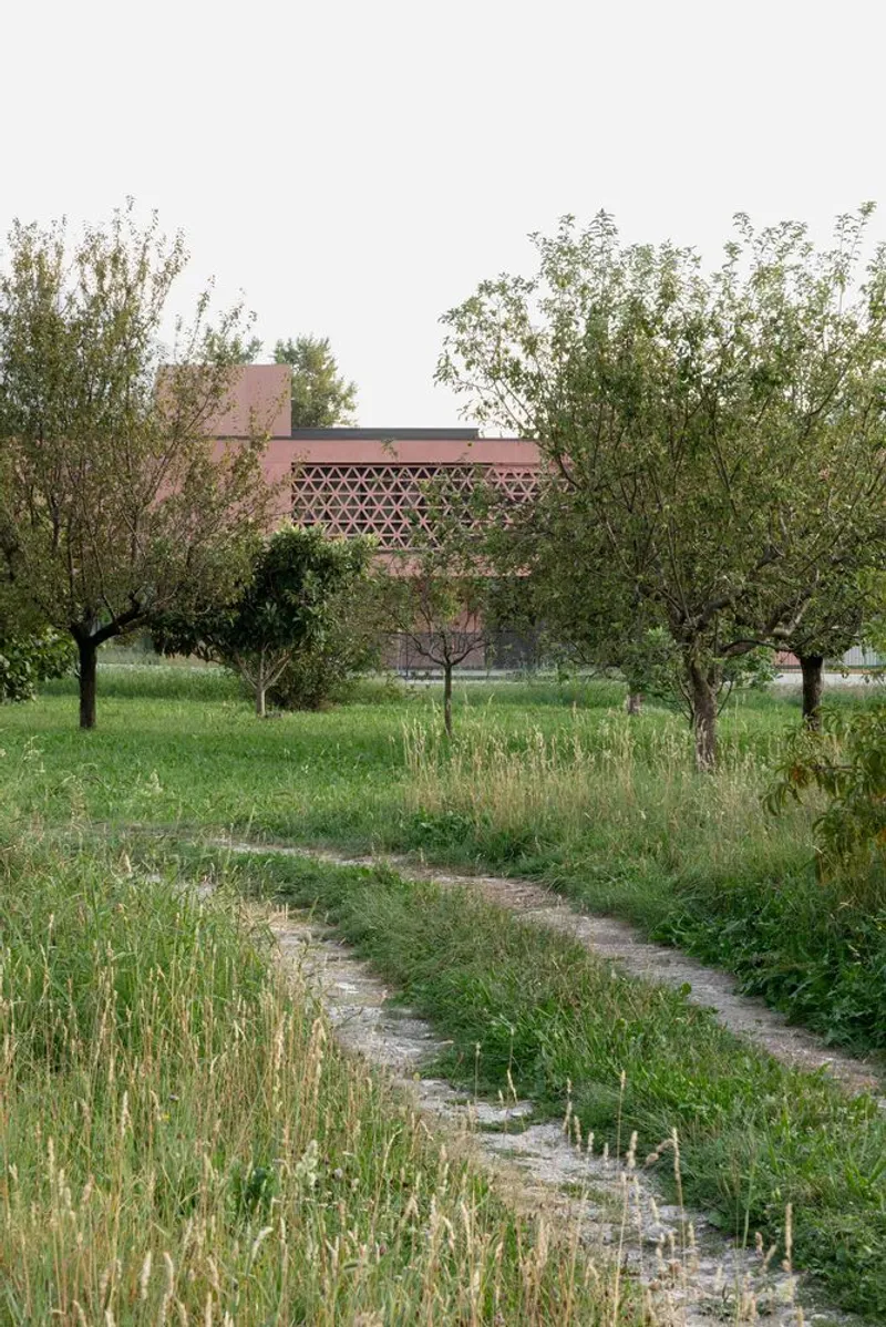 Distant view of the screened facade through an orchard and grassy path