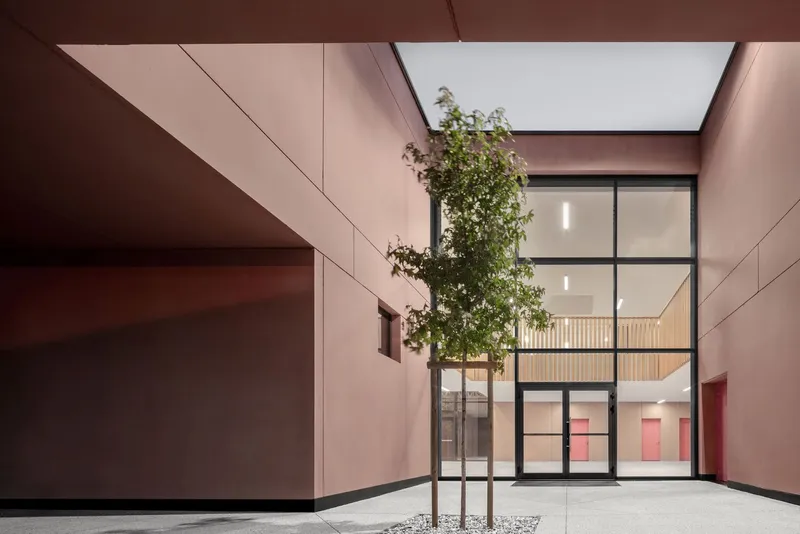 Interior courtyard with a single tree under skylight framed by metal-framed glazing