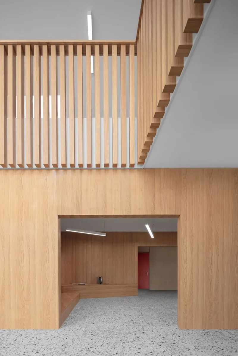 Vertical timber slat screen beneath a cantilevered staircase with white walls and terrazzo floor