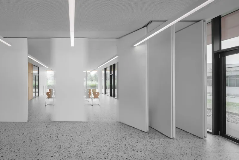 White corridor with sliding partition panels and terrazzo flooring under linear ceiling lights