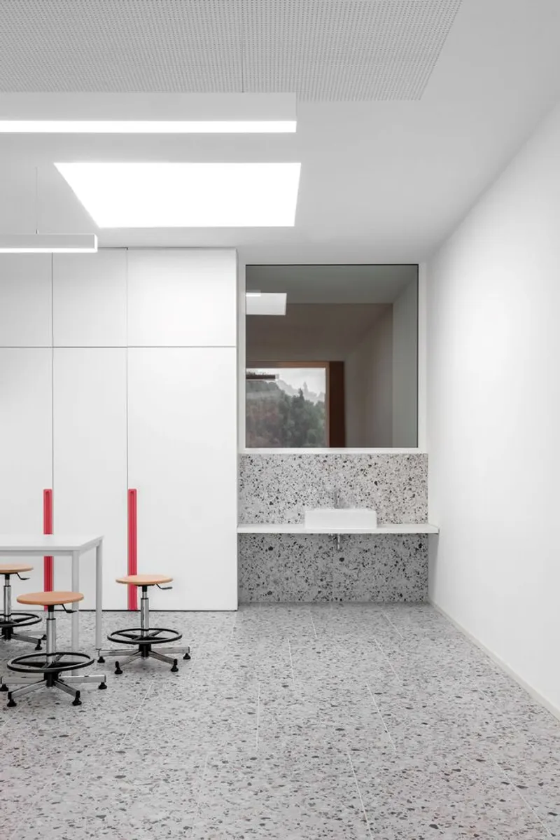 Laboratory workspace with terrazzo countertop, white cabinetry and perforated ceiling with recessed lighting