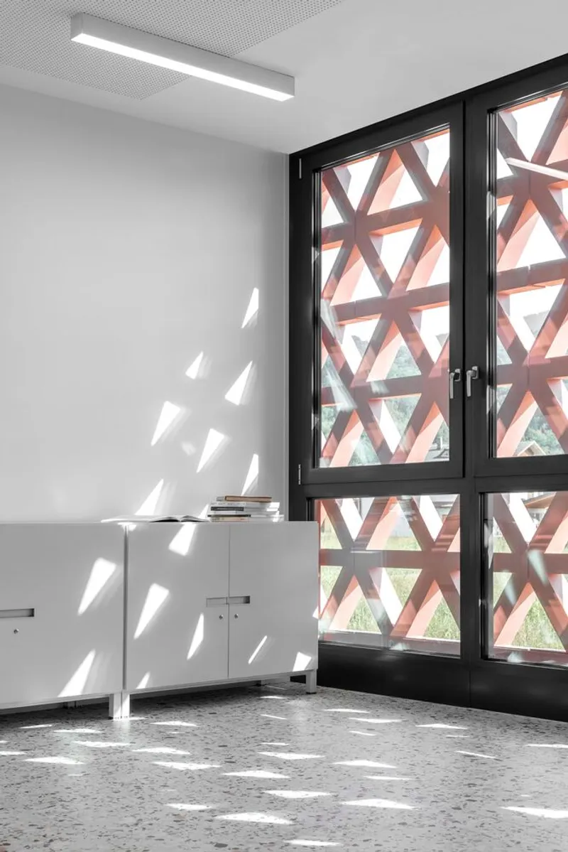 Glazed doors with pink triangular screen casting geometric shadows on white wall and terrazzo floor