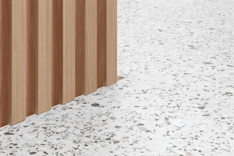 Detail of terrazzo floor meeting vertical timber slat wall with alternating wood tones