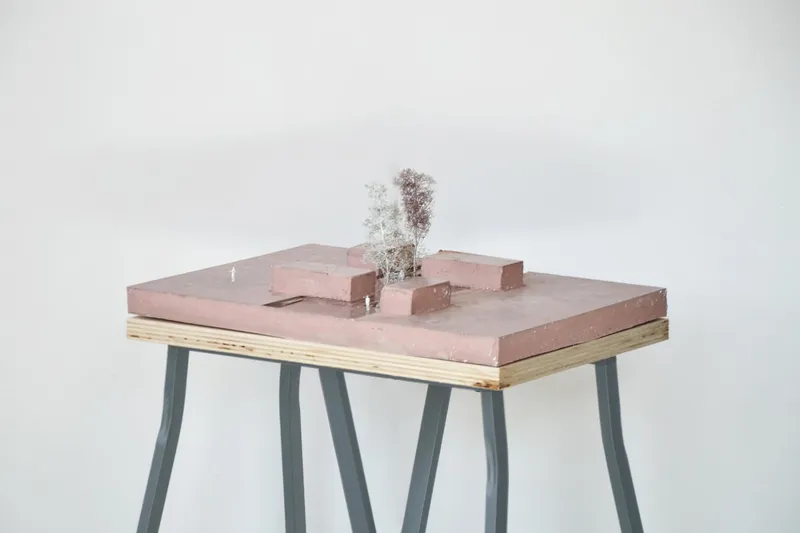 Physical model on plywood base with pink volumes and miniature tree on angled metal legs