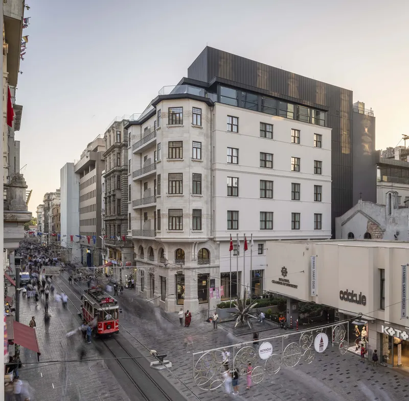 Corner facade with white rendered walls and dark corrugated metal penthouse above a busy pedestrian street