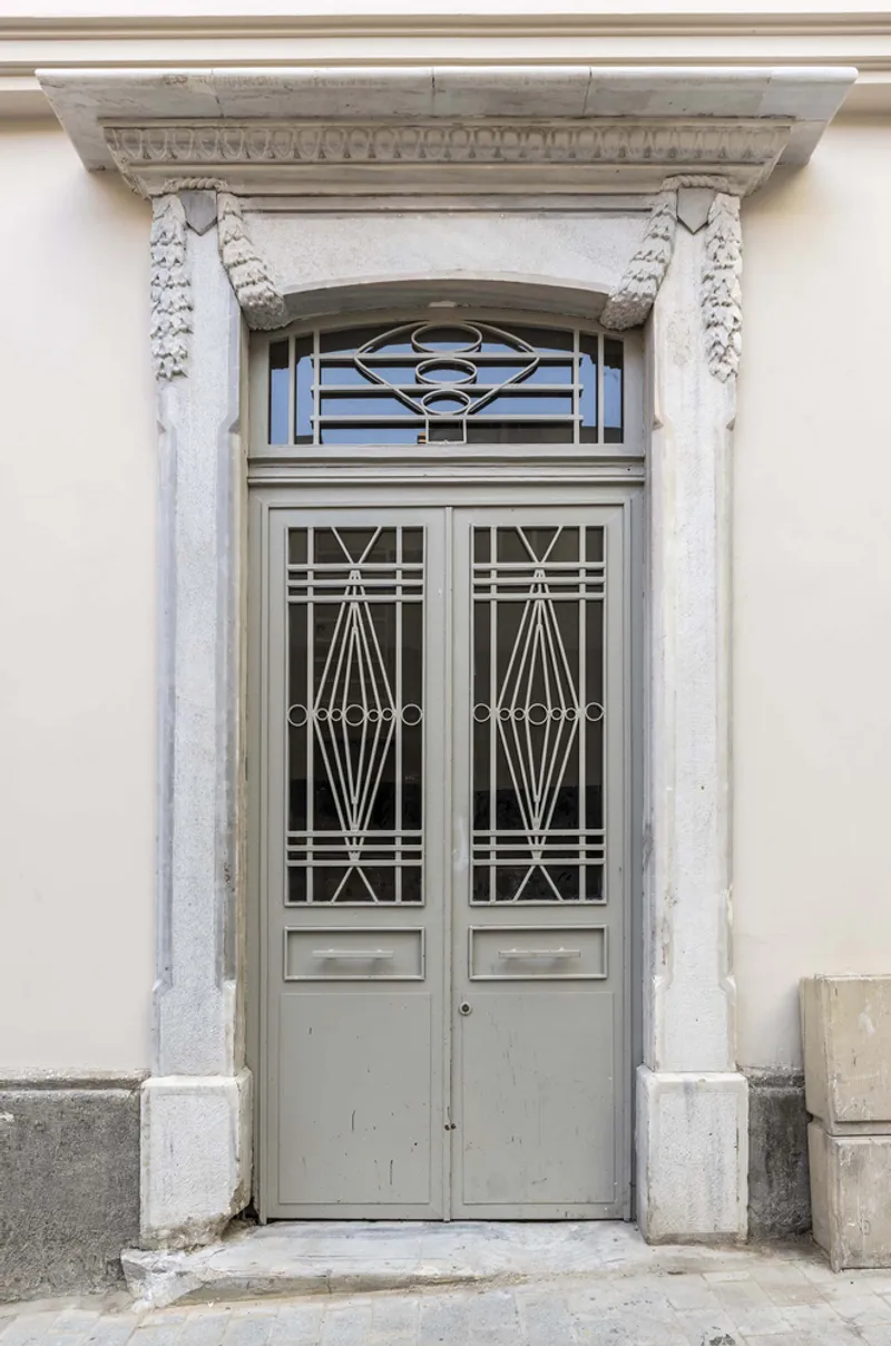 Exterior entrance with carved stone surround, geometric glazed doors, and decorative transom panel