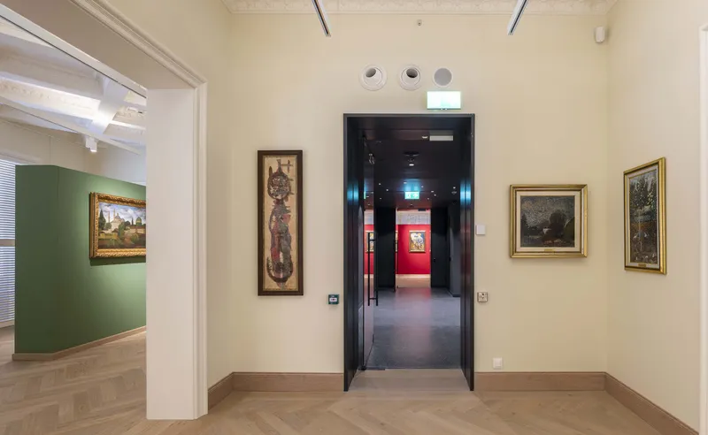 Interior gallery junction with doorways to adjacent rooms and framed artwork on cream walls