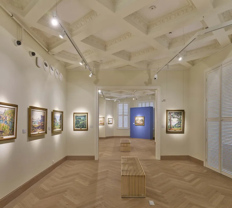 Gallery room with coffered ceiling, herringbone timber floor, and track lighting illuminating framed paintings