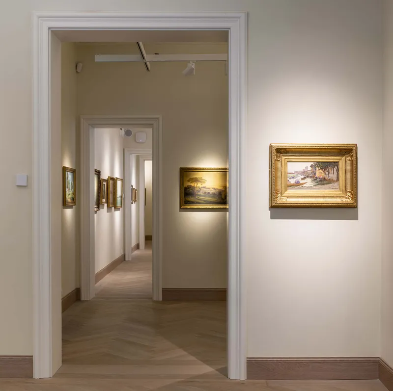 Enfilade of gallery rooms with framed paintings on white walls and herringbone timber flooring