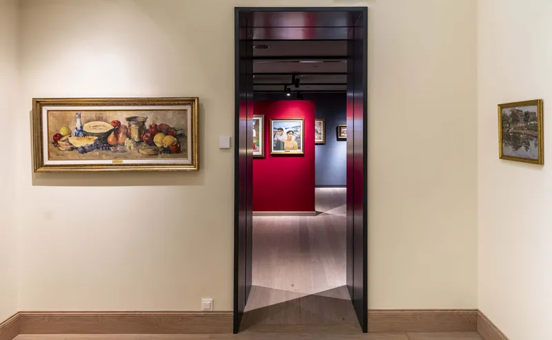 Gallery doorway framed in dark polished timber opening to a red-walled room with framed artworks