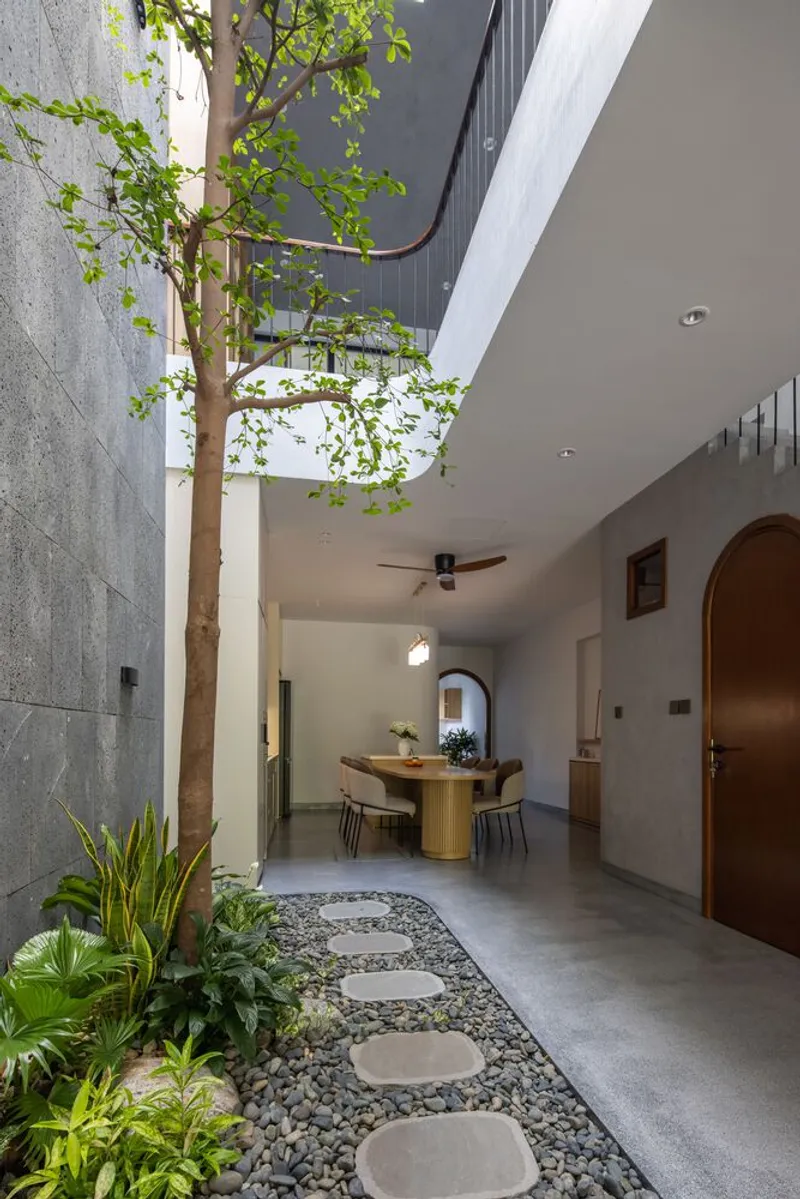 Interior courtyard with stepping stones through pebbles, a planted tree reaching toward the open sky above