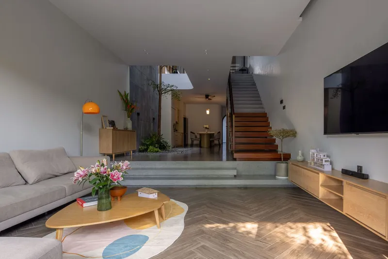 Living room with herringbone floor looking through to timber staircase and interior courtyard with planted tree