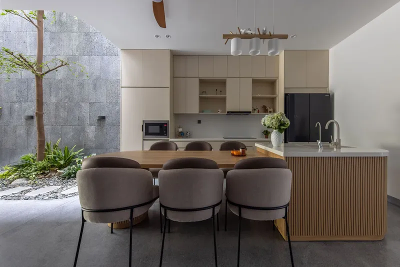 Open kitchen and dining area with fluted timber island facing a courtyard with concrete wall and planted tree