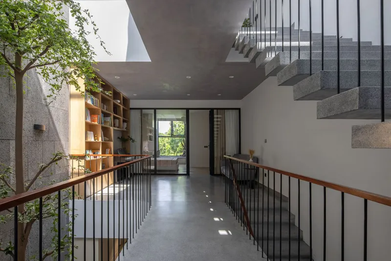 Upper floor landing with timber bookshelf and black metal railings overlooking the courtyard tree below